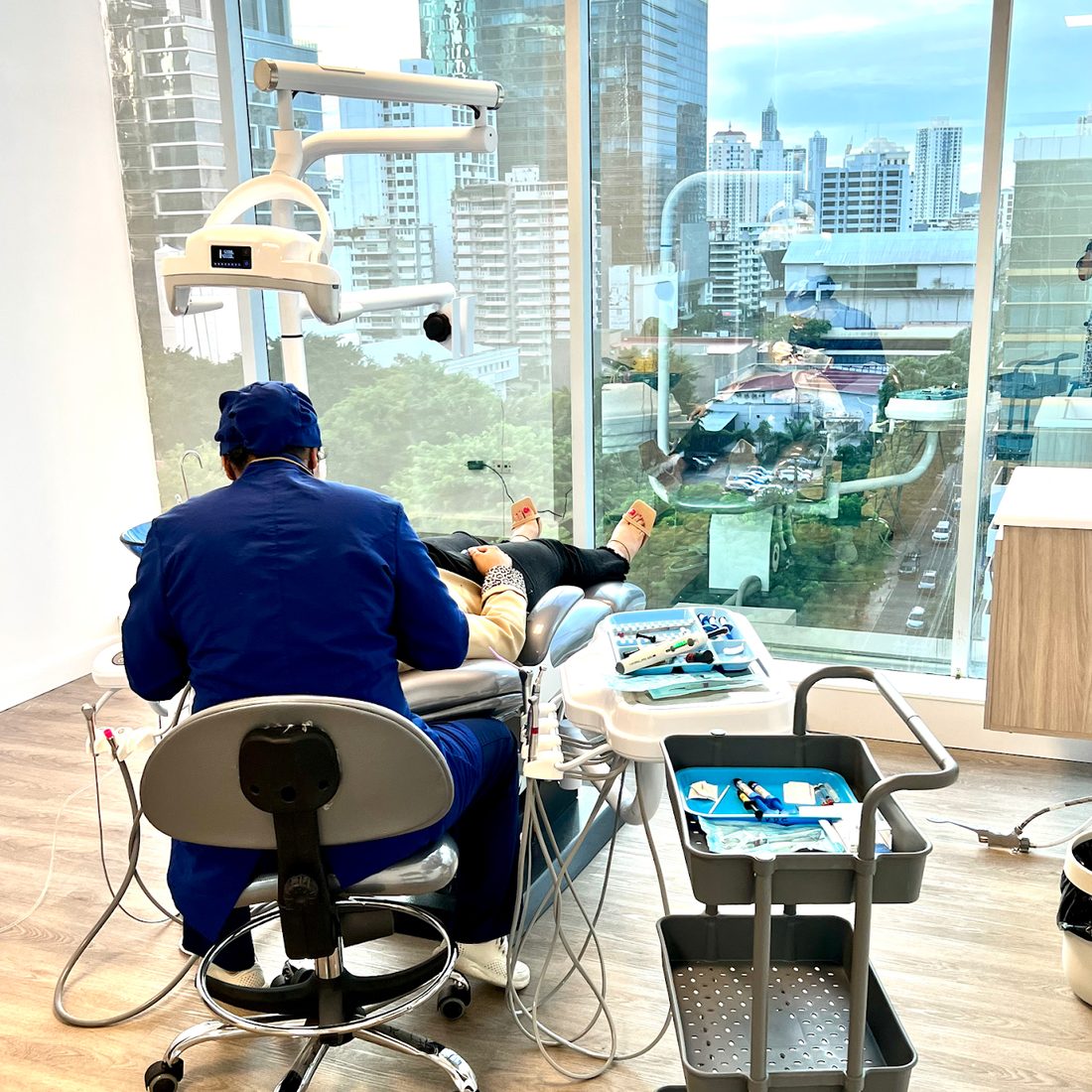 Consultorio de Armonía con ventanal hacia la ciudad, sillón dental y odontólogo atendiendo